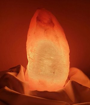Glowing Himalayan salt lamp placed on draped fabric, creating a warm ambiance.